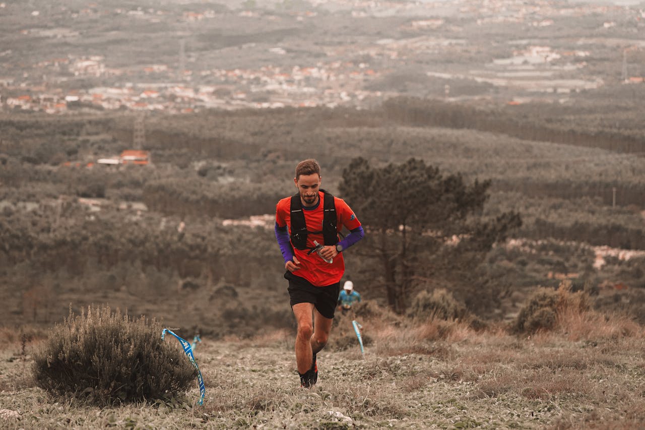 gallery-1 Man running on a mountain trail with scenic landscape in the background.